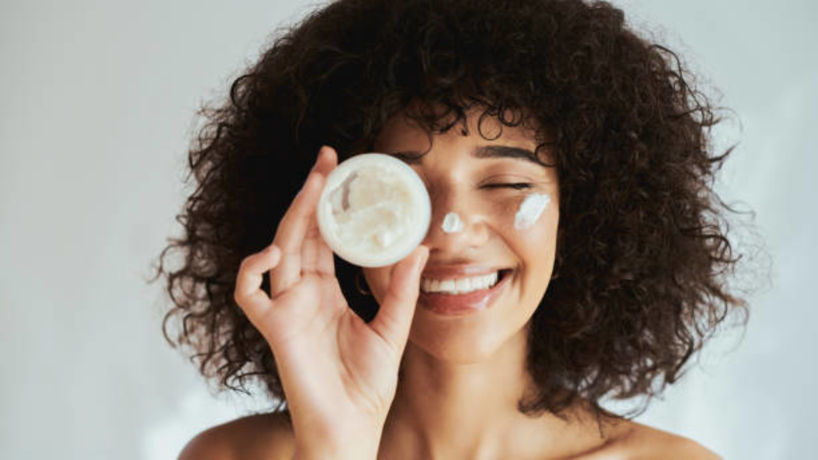 Cream, lotion and face of black woman with beauty product, skincare cosmetics and advertising isolated on white wall. Beautiful skin care person with container, moisturizer and essential oil mockup